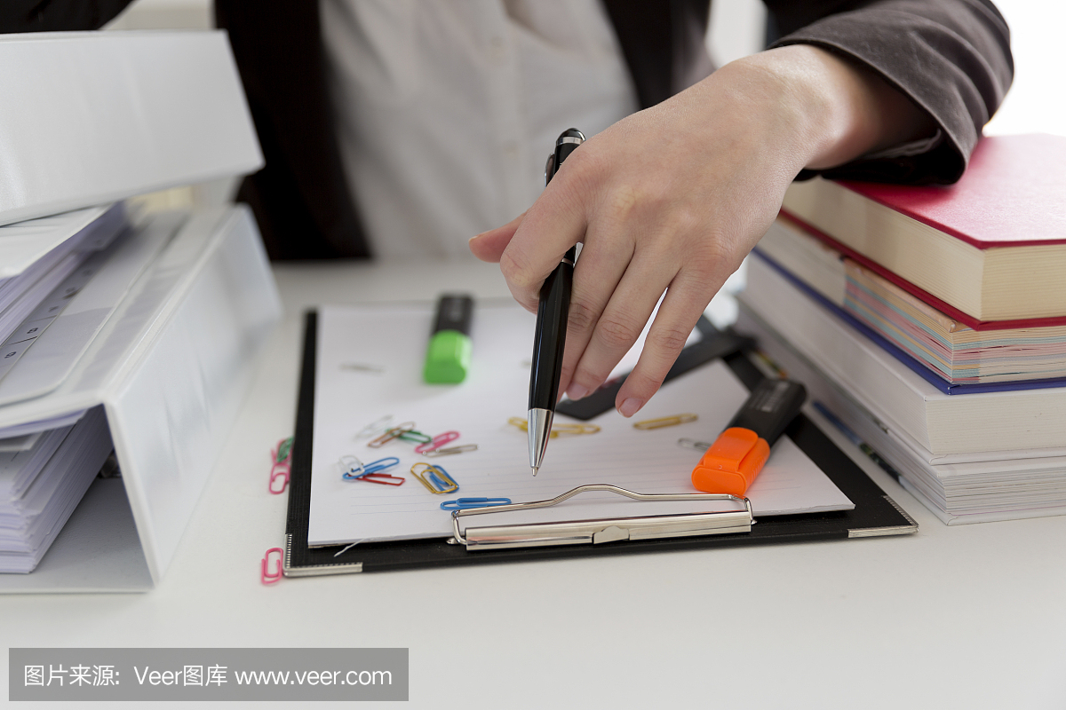 坐在滿是文書,書籍和文件的桌子旁的女人。混亂的工作場所。過載和過度勞累